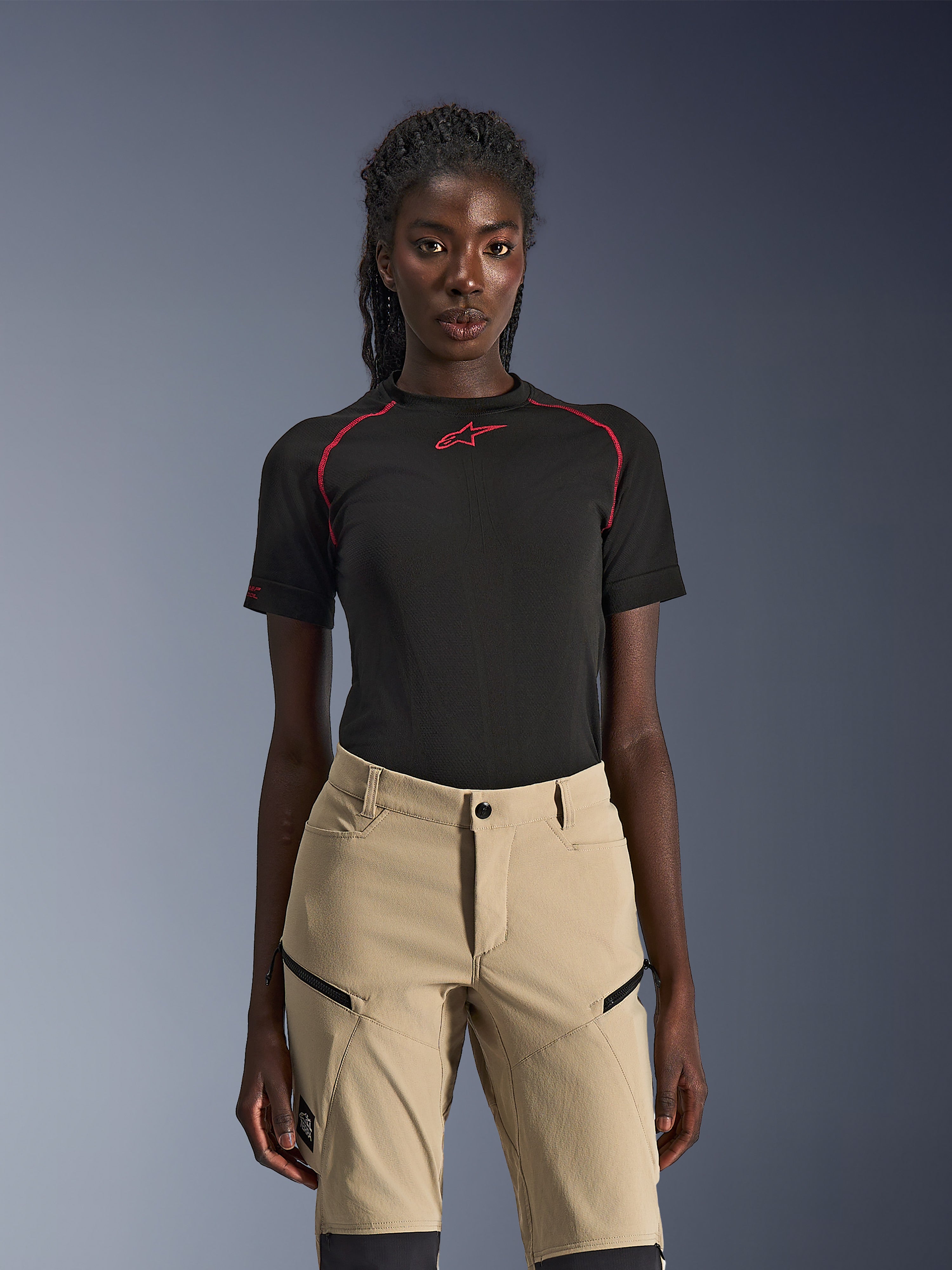 Alpinestars Stella Flex-AST Explorer Pants, pantaloni da moto da donna color sabbia, indossati con un top tecnico nero a maniche corte con cuciture rosse, abbigliamento da adventure touring con tasche cargo con zip e resistente tessuto ripstop.