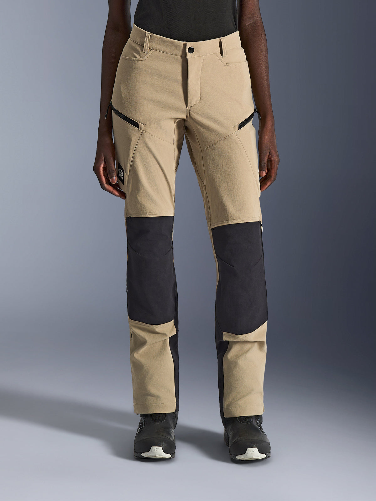 Pantaloni Alpinestars Stella Flex-AST Explorer da donna, pantaloni da moto, Aluminum Black, vista frontale su modella, realizzati in tessuto color sabbia con evidenti pannelli ripstop neri su ginocchia e parte inferiore delle gambe, tasche con cerniera, stile adventure touring
