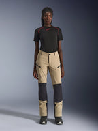 Pantaloni Alpinestars Stella Flex-AST Explorer da donna, pantaloni da moto, color sabbia con pannelli neri, indossati da una modella con maglia nera a maniche corte e stivali neri, dotati di pannelli rinforzati sulle ginocchia, tasche cargo con cerniera e tessuto ripstop traspirante per la guida adventure in climi caldi