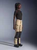 Pantaloni Alpinestars Stella Flex-AST Explorer da donna, pantaloni adventure touring sabbia e nero, profilo laterale su una modella che indossa una t-shirt Alpinestars nera e stivali da moto, dotati di rinforzi in ripstop sulle ginocchia e tasche cargo con cerniera.
