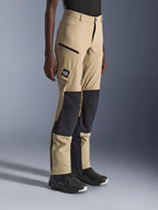 Donna che indossa i pantaloni Alpinestars Stella Flex-AST Explorer, pantaloni da moto adventure color sabbia e nero con pannelli ripstop neri sulle ginocchia, tasche cargo con cerniera, patch con logo 'ALL TERRA' e cerniere sulla parte inferiore della gamba.