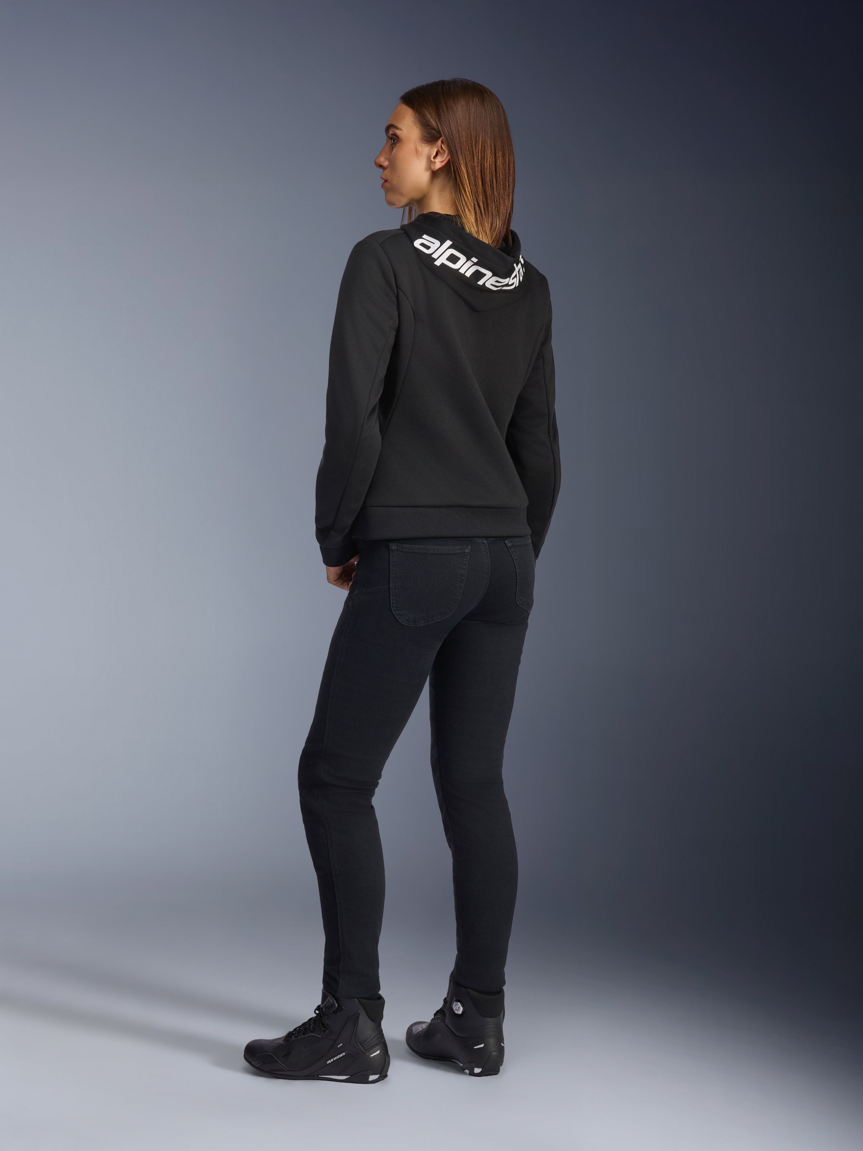 Alpinestars Daisy V3 Women's Riding Denim, pantaloni da moto da donna, Rinse Black, vista posteriore che mostra la vestibilità slim e la vita alta, abbinati a una felpa Alpinestars nera e stivali da moto per un look urban