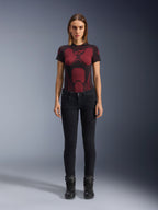 Alpinestars Daisy V3 Women's Riding Denim, pantaloni da moto slim-fit, nero, indossati da una modella con una t-shirt tecnica a motivi rossi e neri e stivali da moto neri, abbigliamento urban riding casual con silhouette femminile e design a vita alta.
