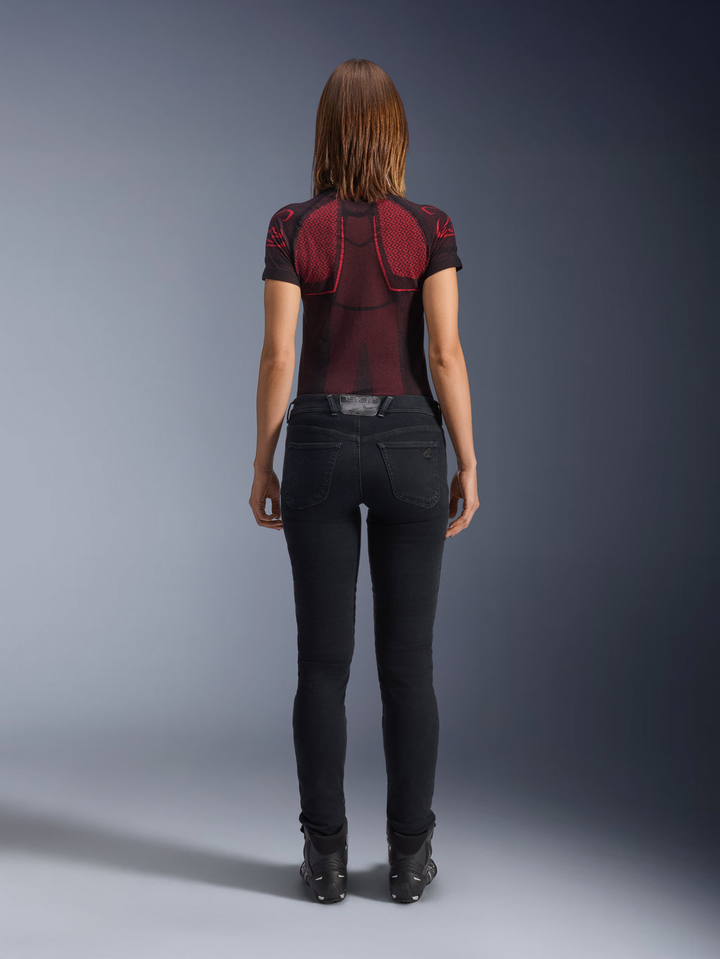 Alpinestars Daisy V3 Women's Riding Denim, Rinse Black, pantaloni da moto slim fit visti da dietro, con design a vita alta e tasche posteriori, abbinati a maglia tecnica rossa e nera e stivali neri, abbigliamento moto urban da donna