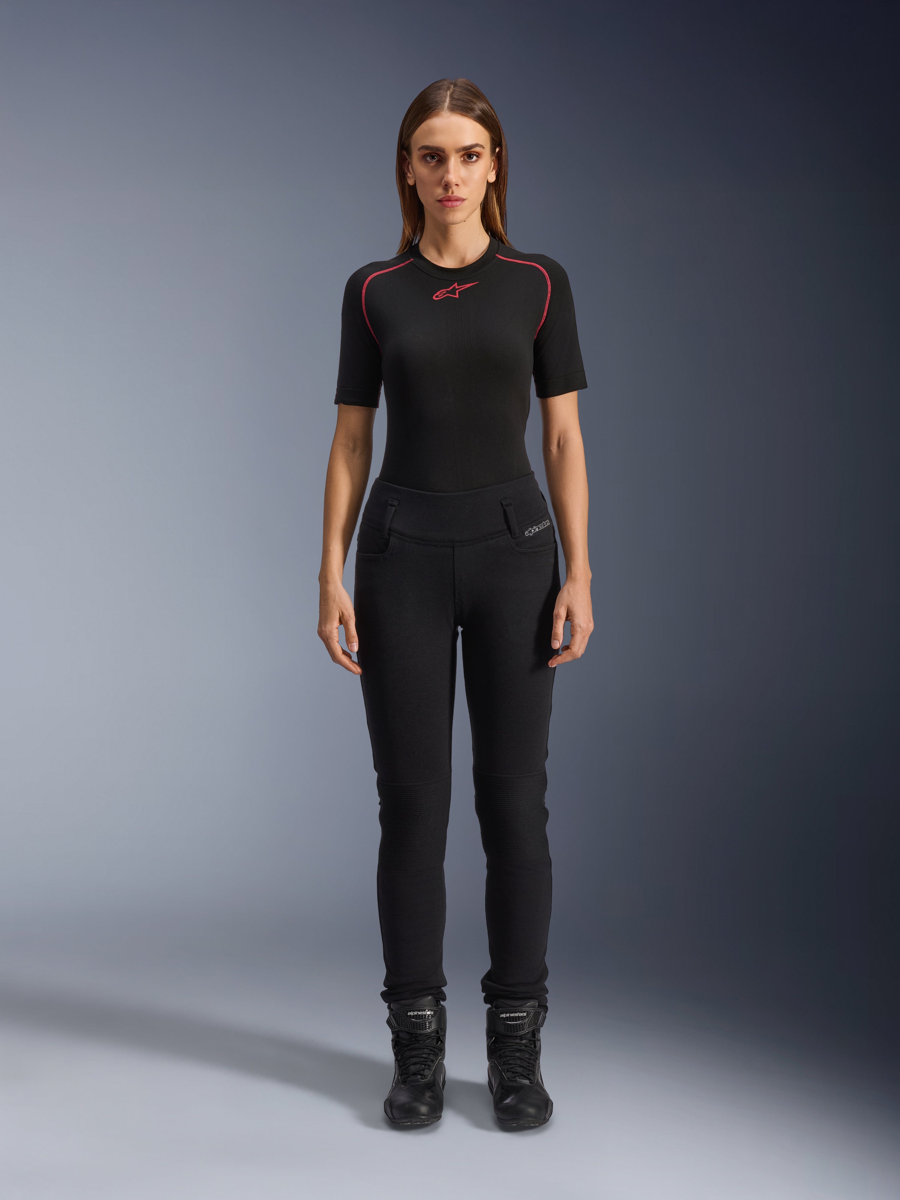 Alpinestars Leggings Banshee Donna, leggings da moto neri, vestibilità anatomica aderente, indossati da una modella con base layer nero e stivali da moto, con pannelli a costine sulle ginocchia e struttura a vita alta per la guida urbana