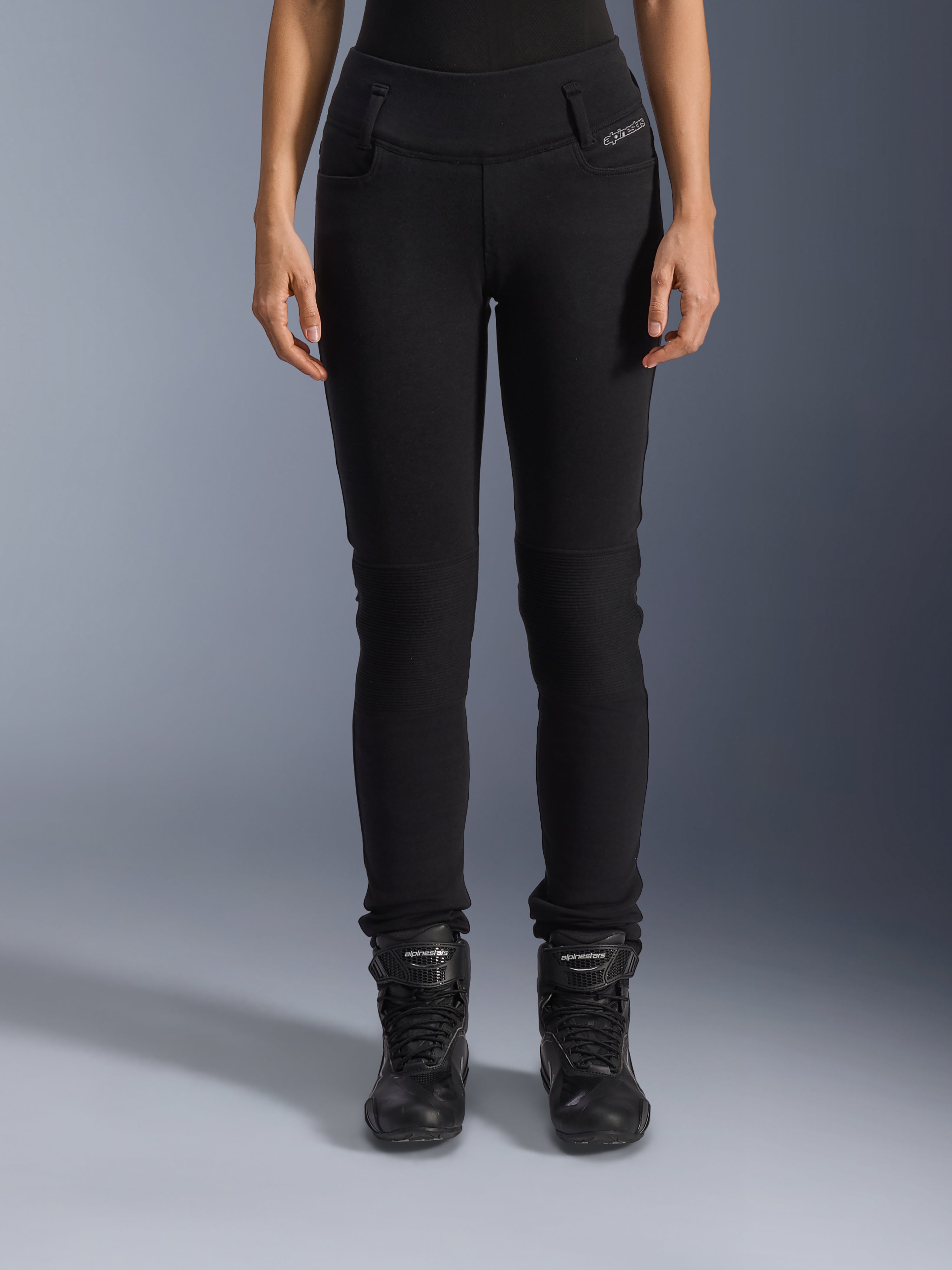 Alpinestars Leggings Banshee Donna, pantaloni da moto neri, design aderente con pannelli a fisarmonica sulle ginocchia, abbinati a stivali da moto alti neri, abbigliamento urban road dallo stile casual
