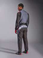 Vista posteriore di un modello che indossa la tuta Alpinestars KMX-9 V3 Graphic 6, tuta da kart, colore antracite, nero e rosso, con l'evidente logo Alpinestars bianco sulla parte bassa della schiena, design a pannelli neri e grigi con accenti rossi, indossata con guanti e scarpe da corsa coordinati.