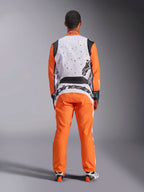 Vista posteriore di un pilota che indossa la tuta Alpinestars KMX-9 V3 Graphic 6 in Bianco Arancione Nero, parte superiore della schiena bianca con grafiche puntinate nere, maniche e pantaloni arancioni, grande marchio Alpinestars nero sulla parte bassa della schiena, coordinata con guanti e stivali da corsa per karting.