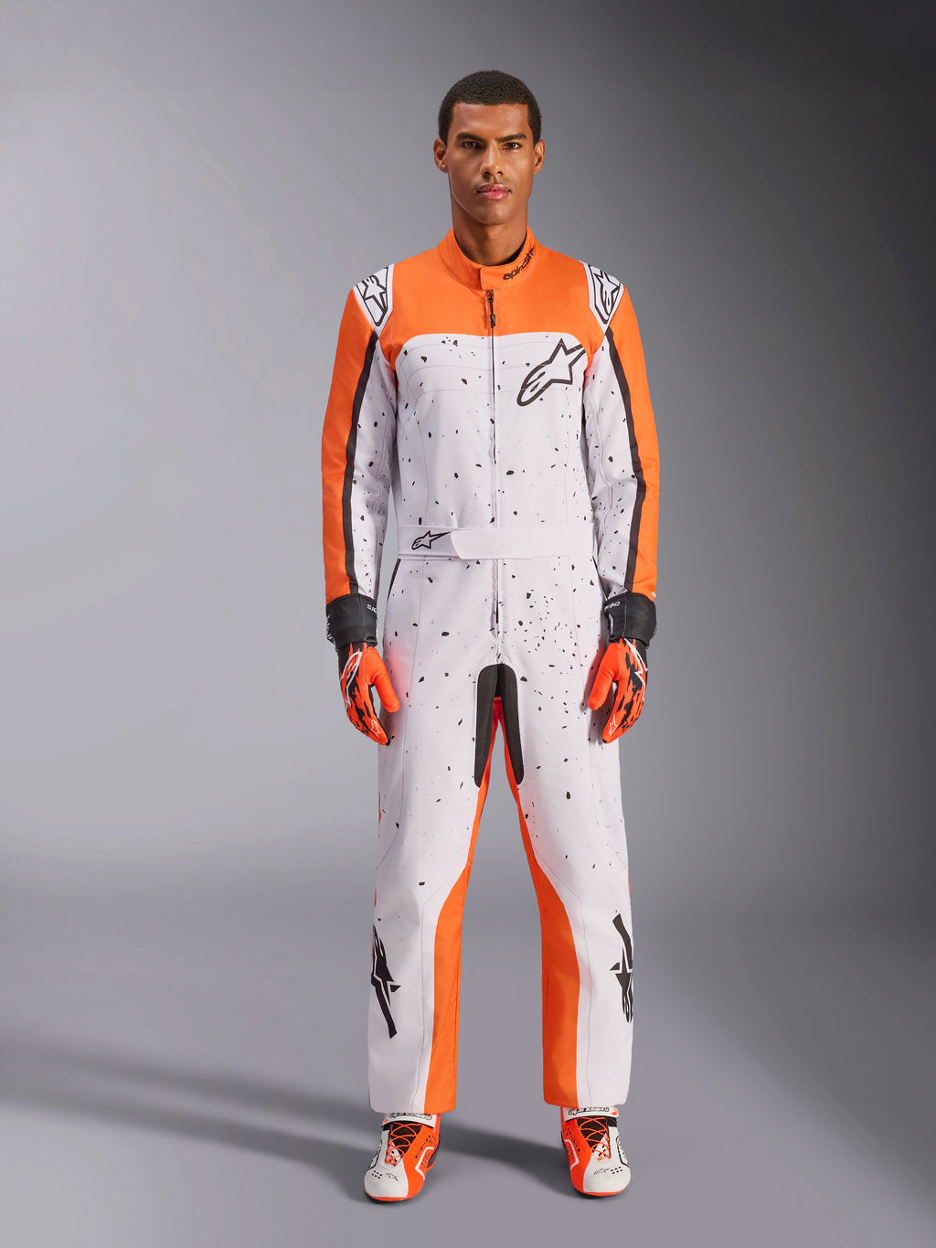 Tuta Alpinestars KMX-9 V3 Graphic 6, tuta da kart, bianco, arancione e nero, con motivo puntinato nero, indossata con guanti e scarpe da corsa coordinati arancioni e neri, equipaggiamento protettivo intero per sport motoristici con loghi audaci e design atletico.