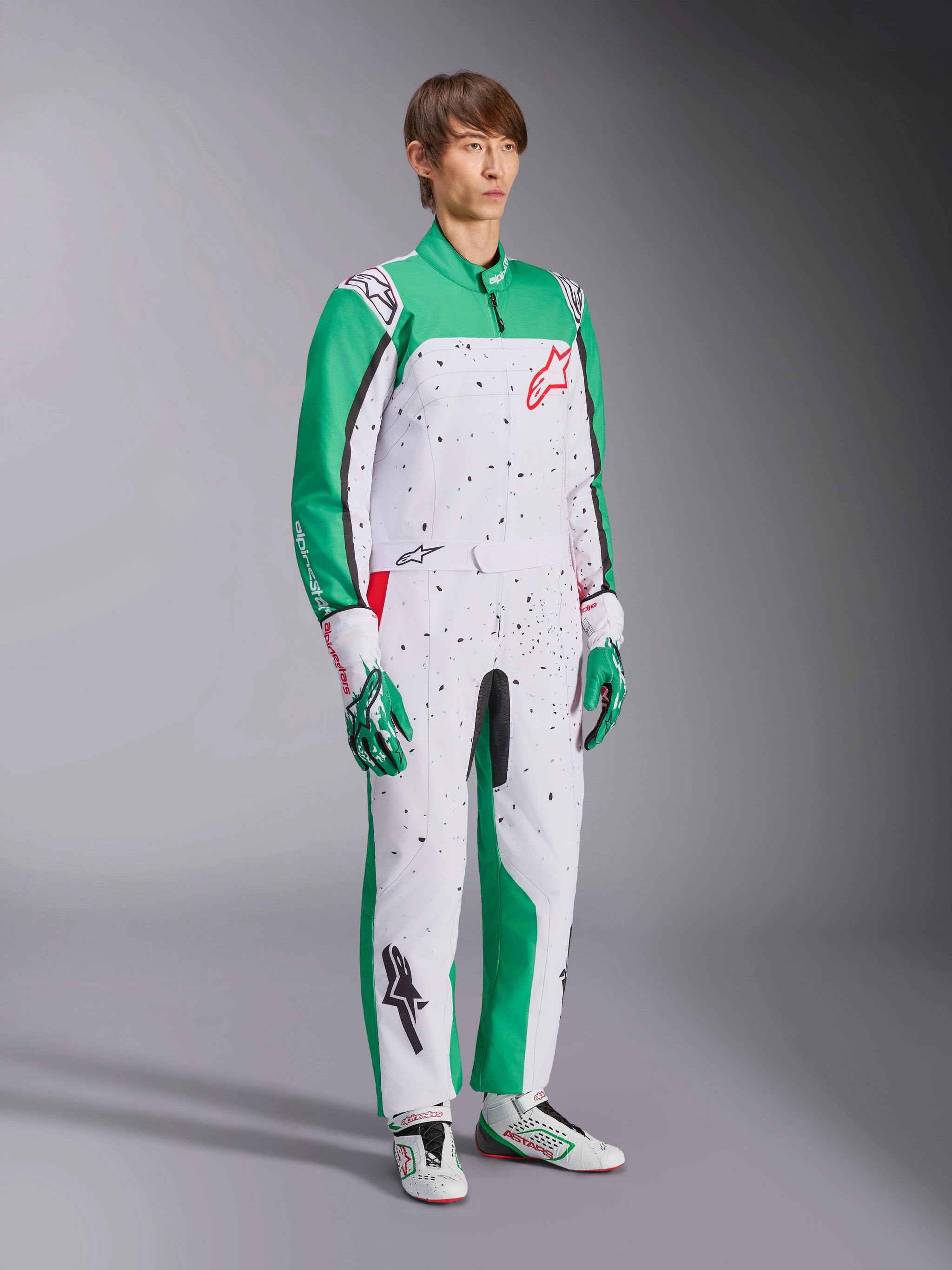 Alpinestars KMX-9 V3 Graphic 6 Suit, tuta da kart, bianco verde e rosso, indossata con guanti e scarpe da corsa coordinati, presenta un corpo bianco con maniche verdi e grafiche con schizzi neri, logo Alpinestars rosso sul petto, design atletico a pezzo unico per il motorsport.