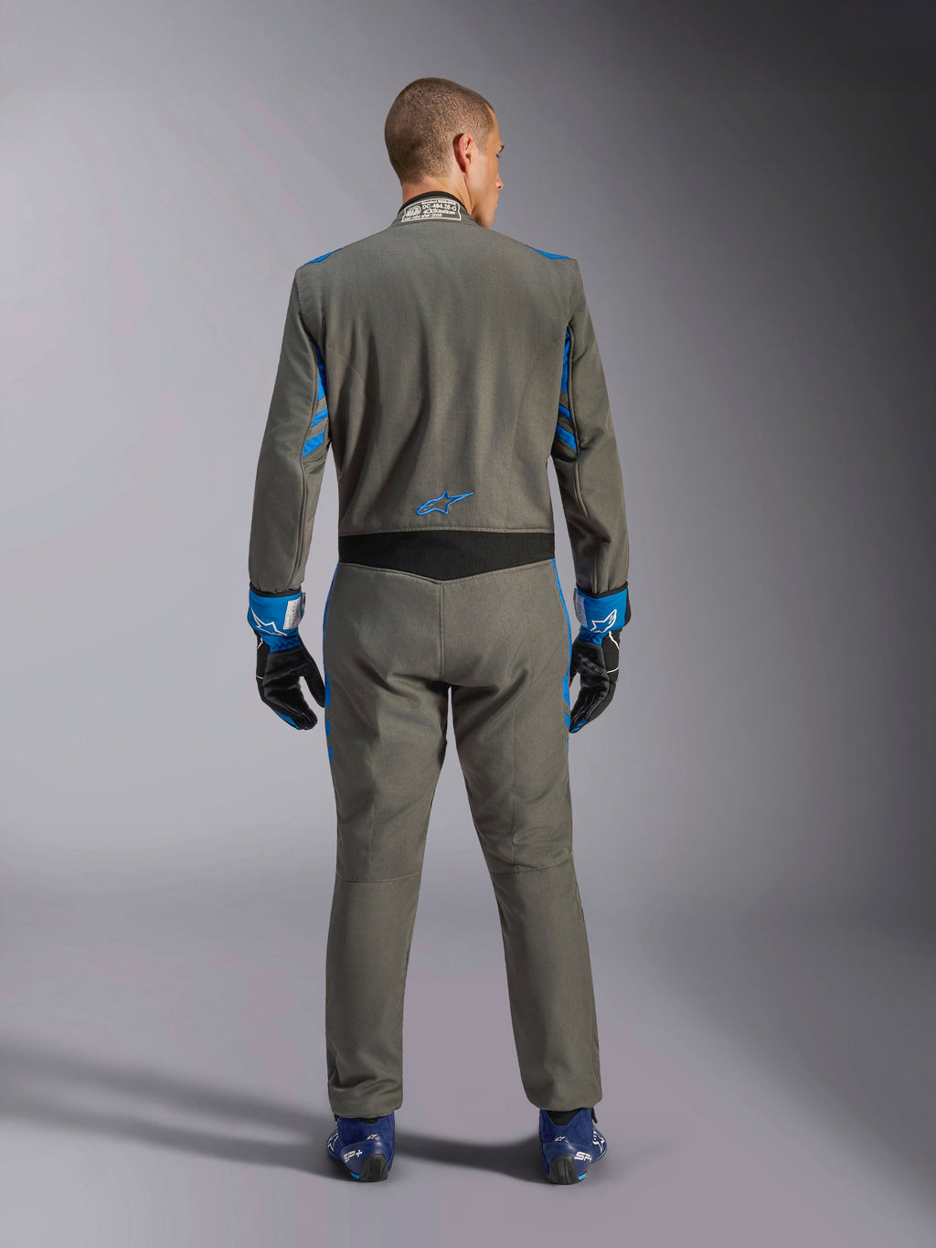 Tuta Alpinestars GP Race V3 FIA, vista posteriore, Blu Antracite con vivaci dettagli blu su braccia e spalle, logo a stella blu sulla parte bassa della schiena, indossata con guanti da corsa abbinati e scarpe blu, tuta professionale per gare automobilistiche