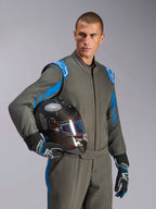 Pilota Alpinestars con tuta GP Race V3 FIA in Anthracite Blue, casco da corsa in fibra di carbonio con visiera iridescente, abbigliamento professionale per corse auto con dettagli blu sulle spalle e guanti coordinati.