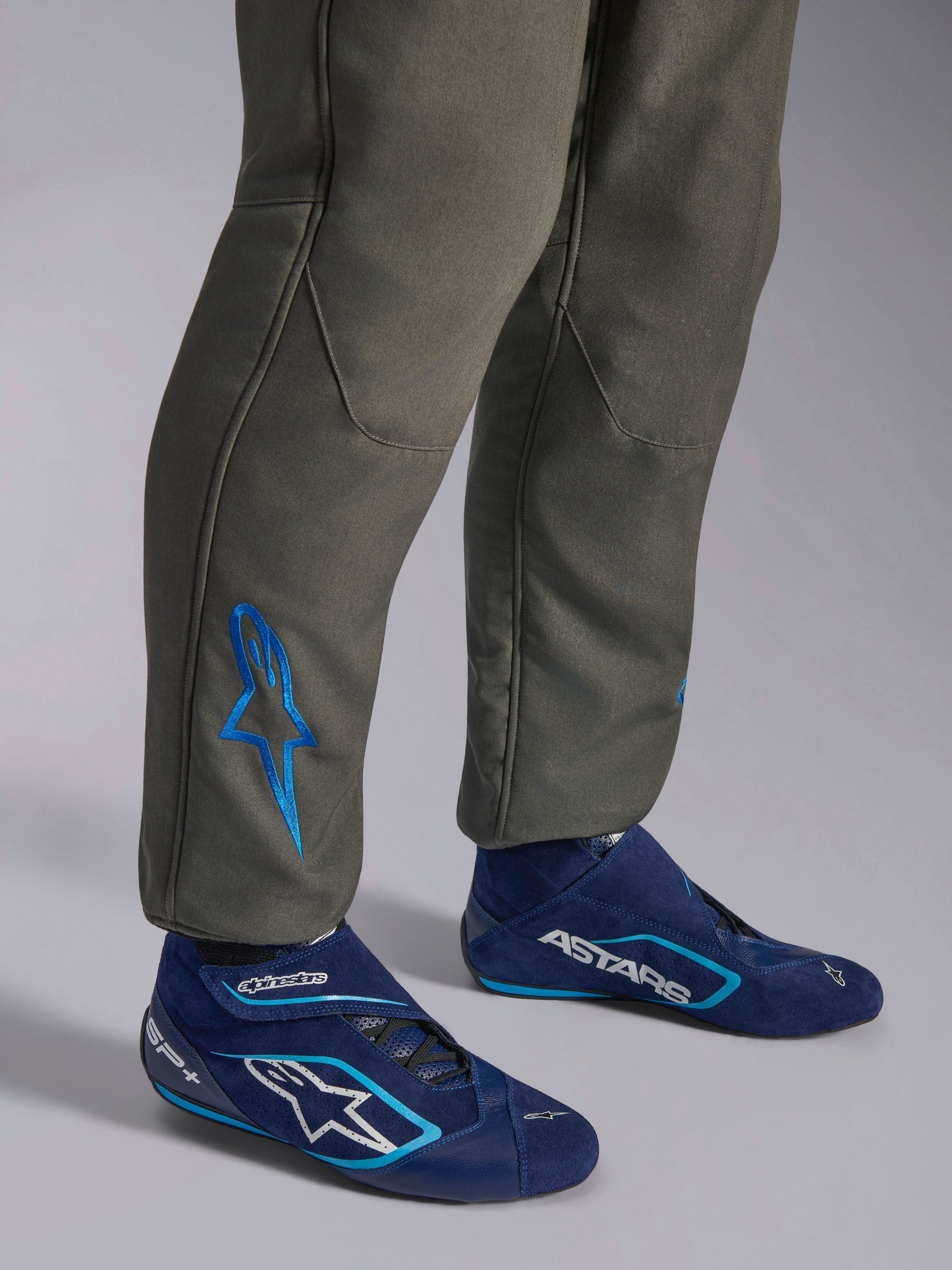 Tuta Alpinestars GP Race V3 FIA, tuta da corsa auto color Anthracite Blue, primo piano della parte inferiore delle gambe con logo Astars ricamato in blu sulla caviglia, abbinata a stivali da gara blu navy e ciano, abbigliamento protettivo professionale per motorsport