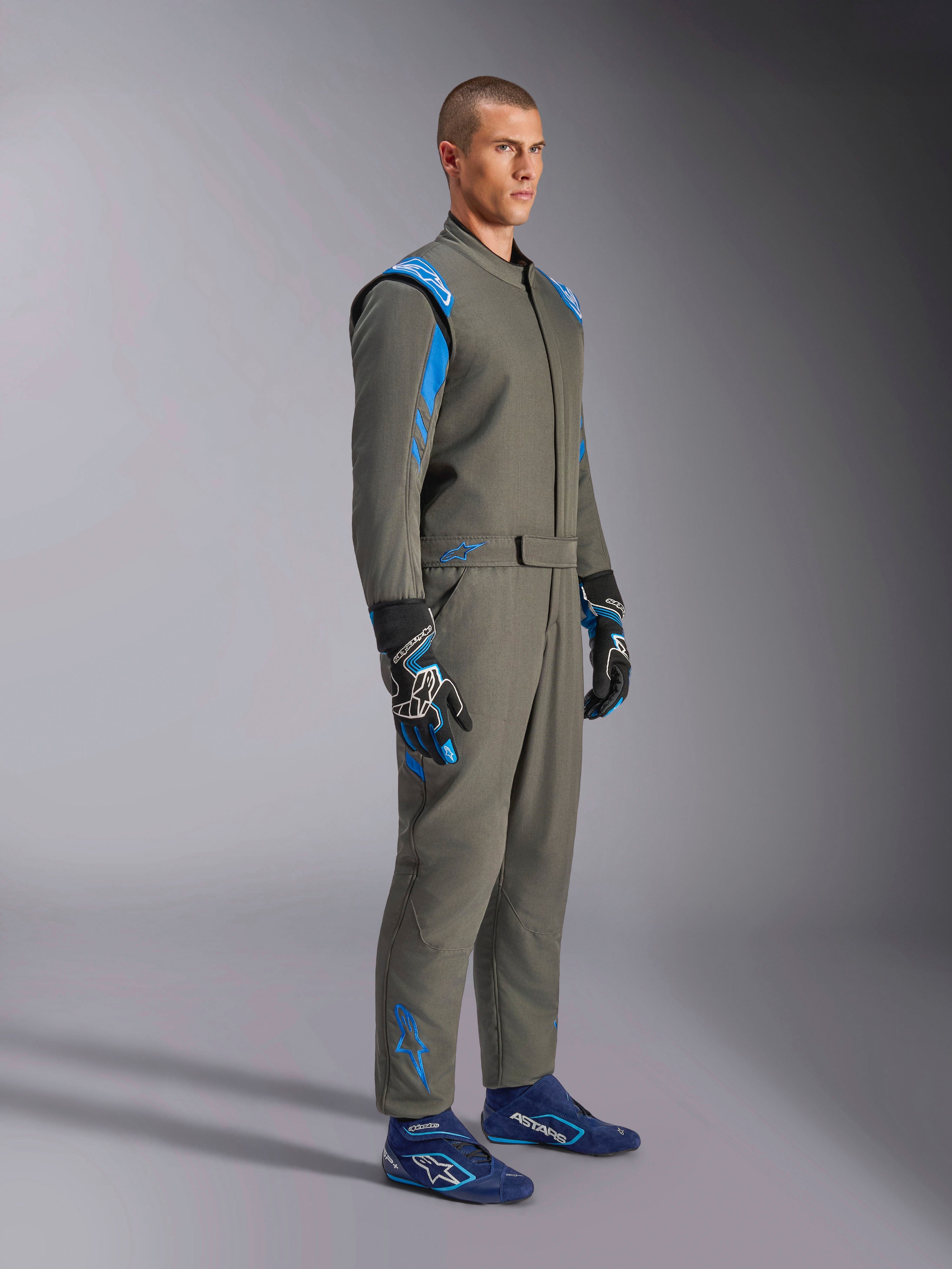 Tuta Alpinestars GP Race V3 FIA in Antracite Blu, tuta intera da corsa indossata da un modello, caratterizzata da accenti blu brillante su spalle e caviglie, abbinata a guanti da corsa coordinati e scarpe da corsa blu, equipaggiamento professionale per motorsport.