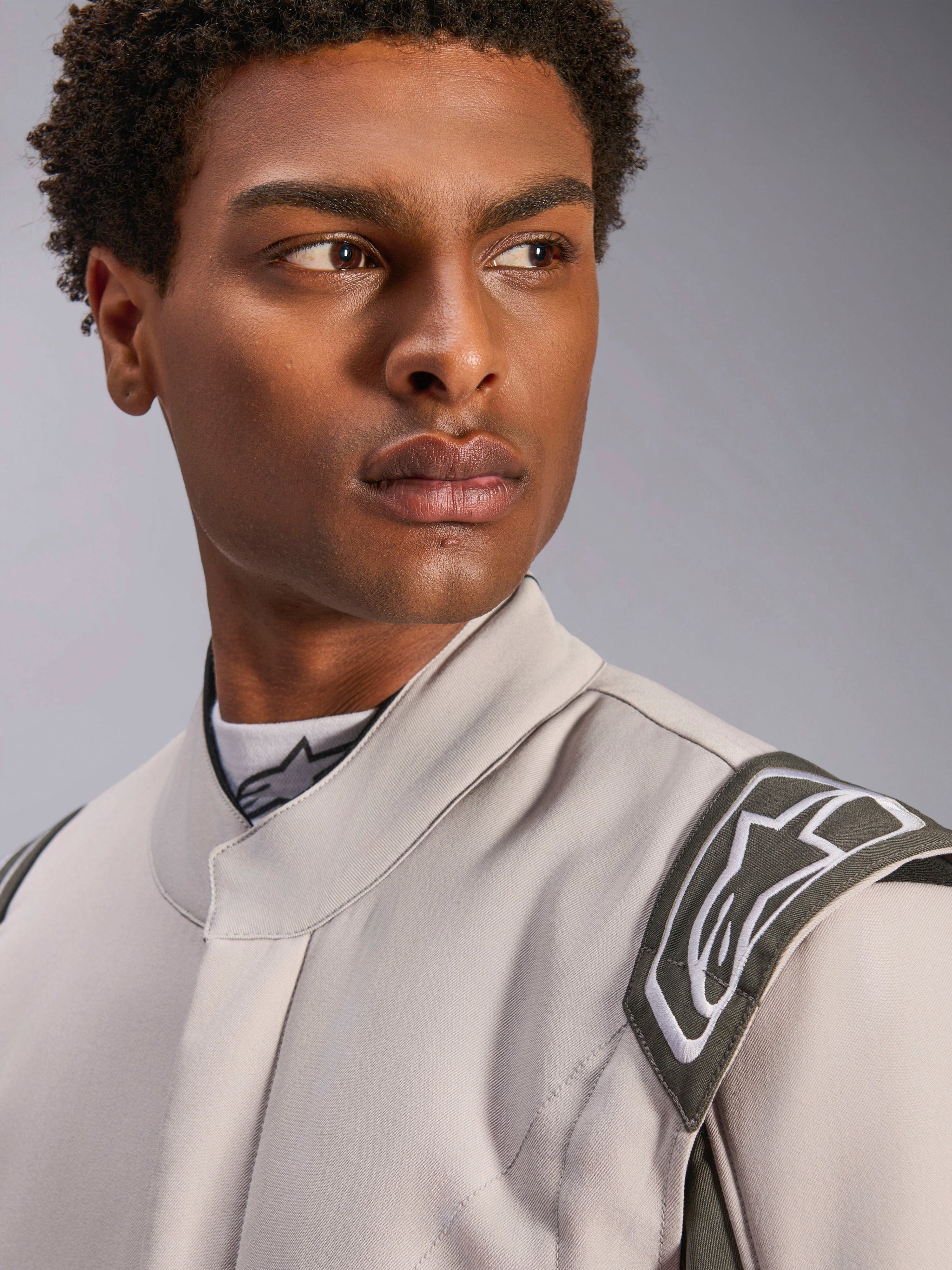 Modello che indossa la tuta Alpinestars GP Race V3 FIA in Silver Anthracite, primo piano focalizzato sulla parte superiore del busto e sulla spalla, che mostra l'epaulette di estrazione e il colletto ergonomico, abbigliamento professionale per corse automobilistiche