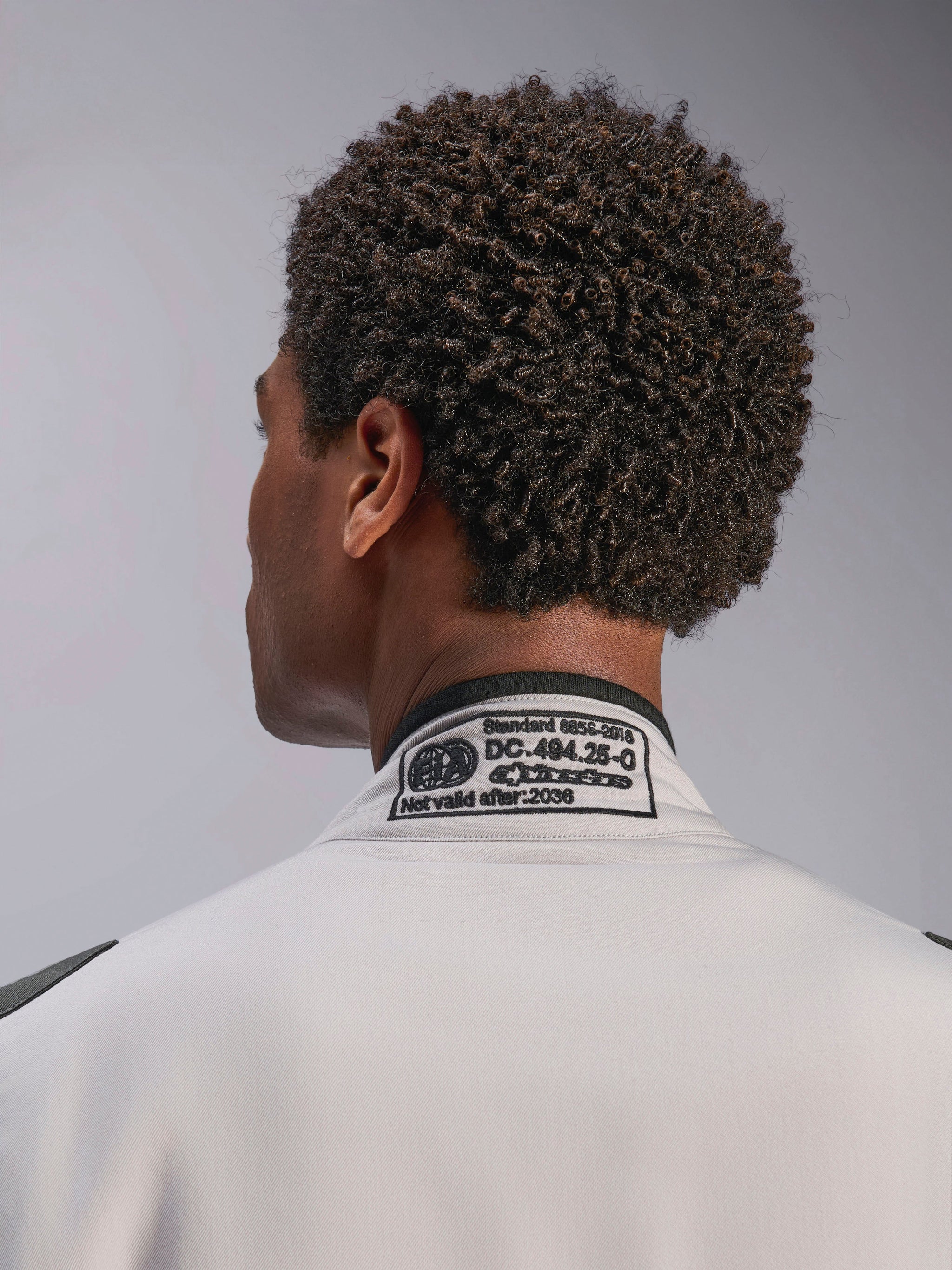 Alpinestars Tuta GP Race V3 FIA, Silver Anthracite, primo piano del colletto posteriore con l'etichetta di certificazione FIA 8856-2018 ricamata, che attesta la conformità di sicurezza per l'abbigliamento da gara automobilistica.