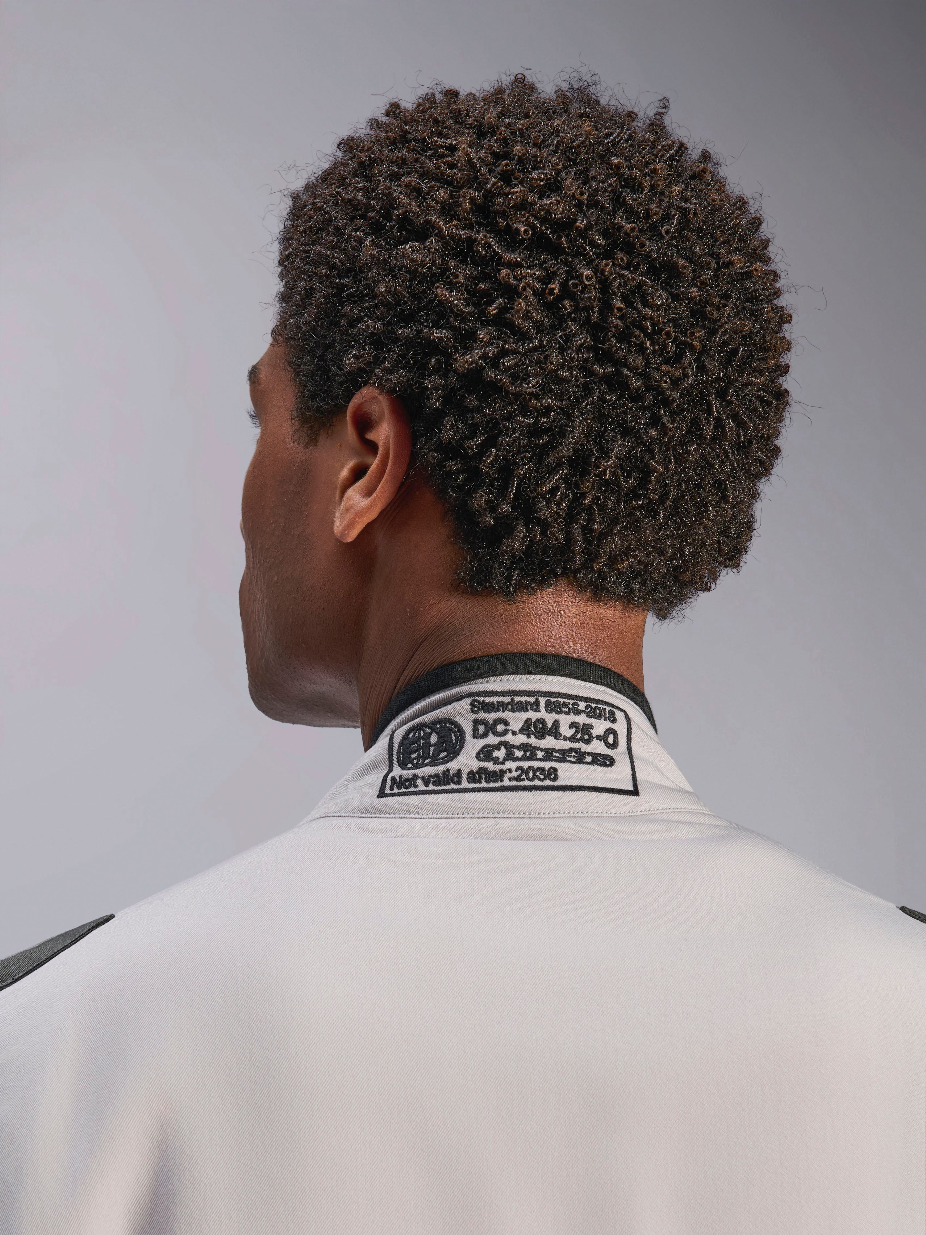 Alpinestars Tuta GP Race V3 FIA, Silver Anthracite, primo piano del colletto posteriore con l'etichetta di certificazione FIA 8856-2018 ricamata, che attesta la conformità di sicurezza per l'abbigliamento da gara automobilistica.