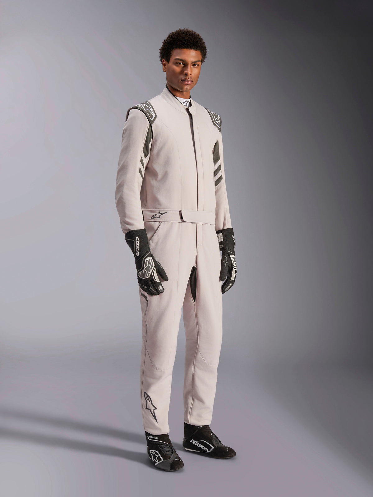 Alpinestars Tuta GP Race V3 FIA, tuta da corsa Silver Anthracite, tuta intera da pilota con spalline e cintura in vita, indossata con guanti e stivali da corsa coordinati neri e bianchi, design elegante per automobilismo professionale