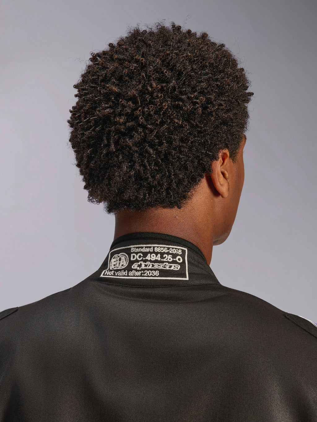 Alpinestars Tuta GP Race V3 FIA, tuta da corsa nera, primo piano dello scollo posteriore con patch di certificazione FIA 8856-2018, vista dettagliata dell'omologazione di sicurezza e logo Alpinestars, abbigliamento per motorsport ad alte prestazioni