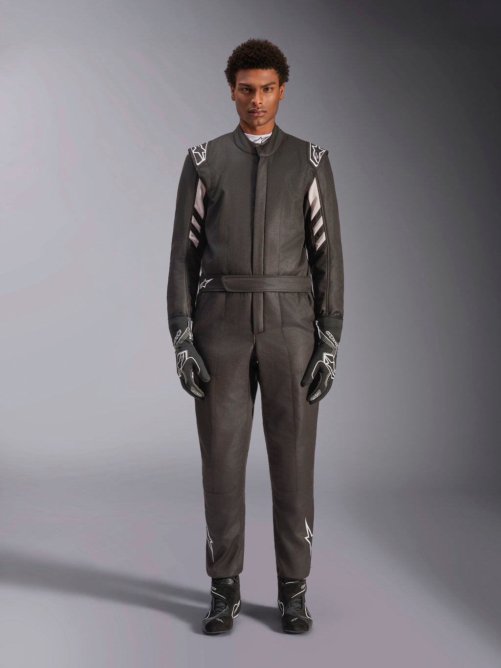 Alpinestars Tuta GP Race V3 FIA, tuta da auto, nero e argento, vista frontale del pilota con attrezzatura da gara completa inclusi guanti e stivali, design professionale per motorsport con logo Alpinestars sulle spalle e sulla cintura