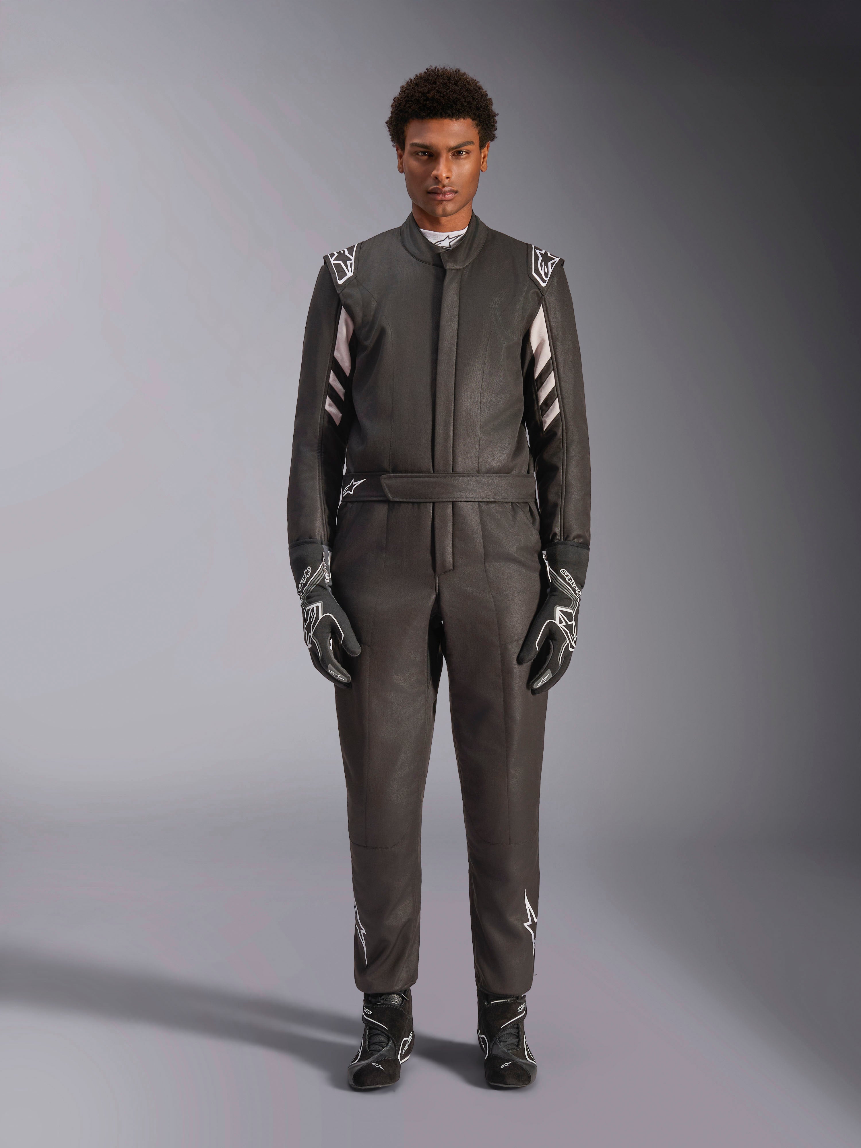 Alpinestars Tuta GP Race V3 FIA, tuta da auto, nero e argento, vista frontale del pilota con attrezzatura da gara completa inclusi guanti e stivali, design professionale per motorsport con logo Alpinestars sulle spalle e sulla cintura