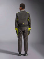 Alpinestars GP Race V3 Suit FIA, vista posteriore, nero con accenti giallo fluo, con pannelli gialli sulle braccia e sul busto, logo giallo sulla parte bassa della schiena, indossata con guanti e stivali da corsa abbinati, tuta professionale da corsa automobilistica