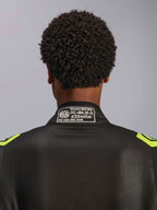 Tuta Alpinestars GP Race V3 FIA, nero e giallo fluo, primo piano del colletto posteriore con etichetta di certificazione FIA 8856-2018, tuta da corsa automobilistica professionale.