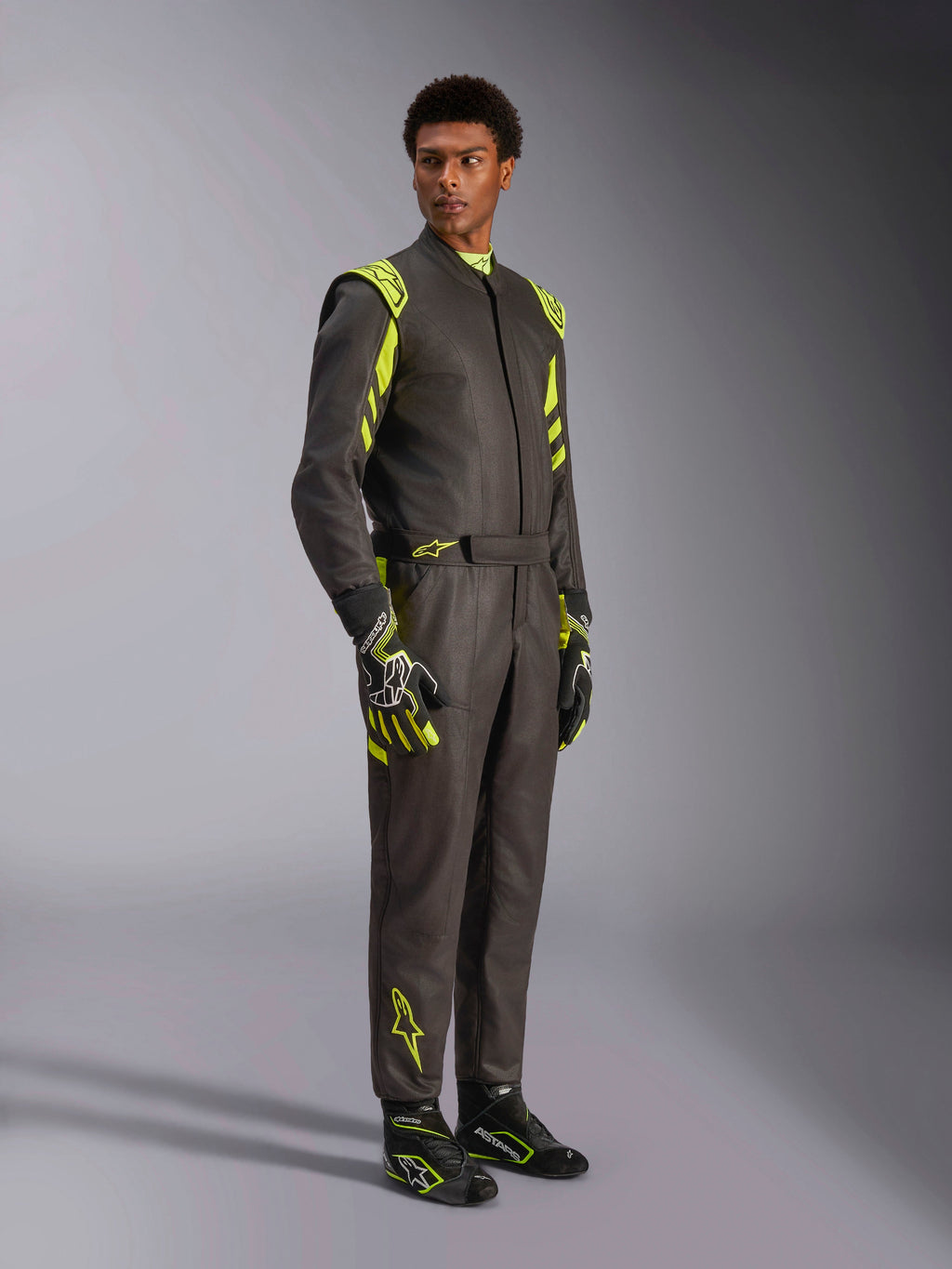 Alpinestars GP Race V3 Suit FIA, tuta da corsa auto, nero e giallo fluo, indossata da un modello con guanti e stivali da corsa abbinati, con vivaci accenti gialli sulle spalle e sulle gambe, attrezzatura professionale per motorsport