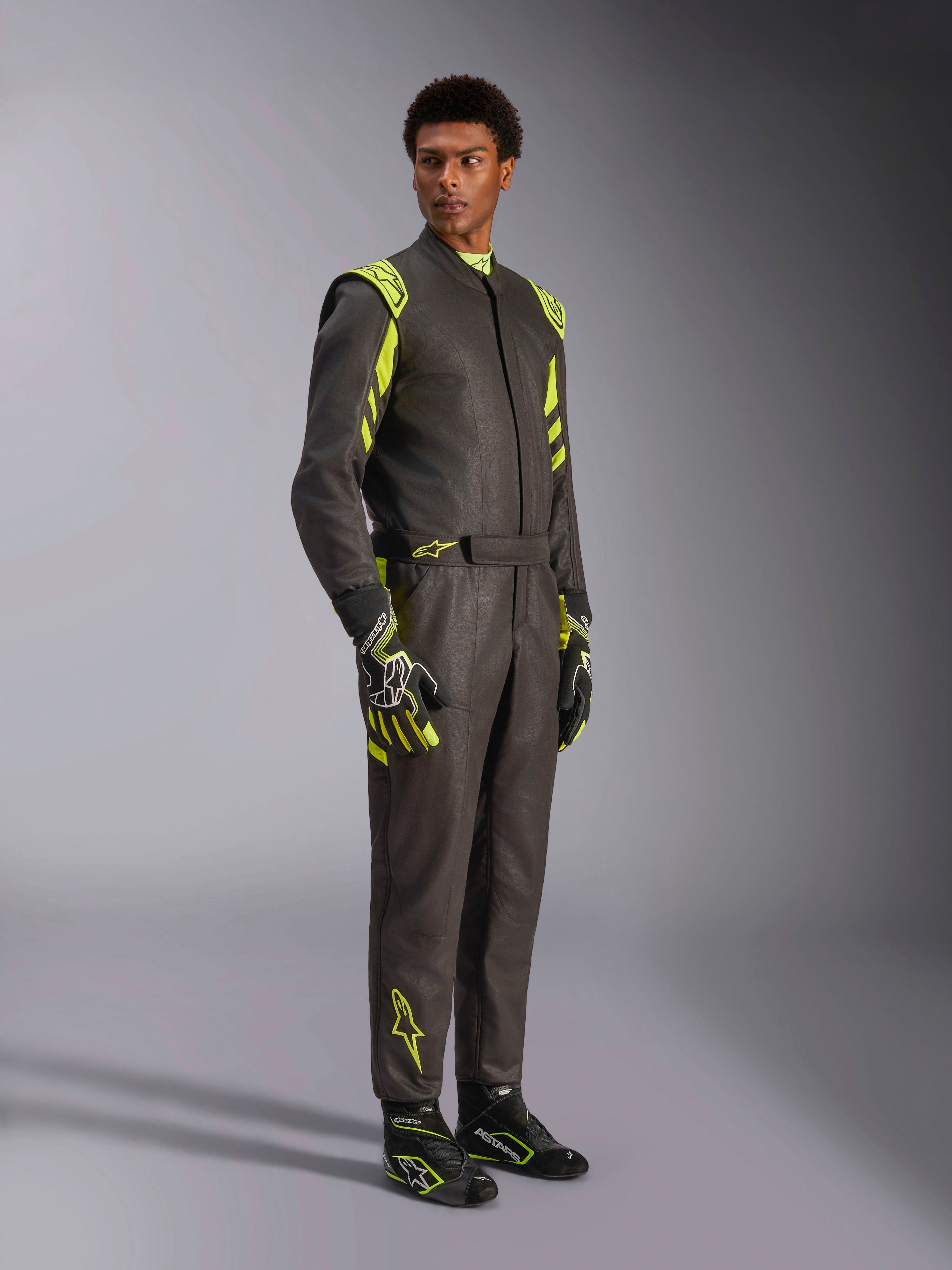 Alpinestars GP Race V3 Suit FIA, tuta da corsa auto, nero e giallo fluo, indossata da un modello con guanti e stivali da corsa abbinati, con vivaci accenti gialli sulle spalle e sulle gambe, attrezzatura professionale per motorsport