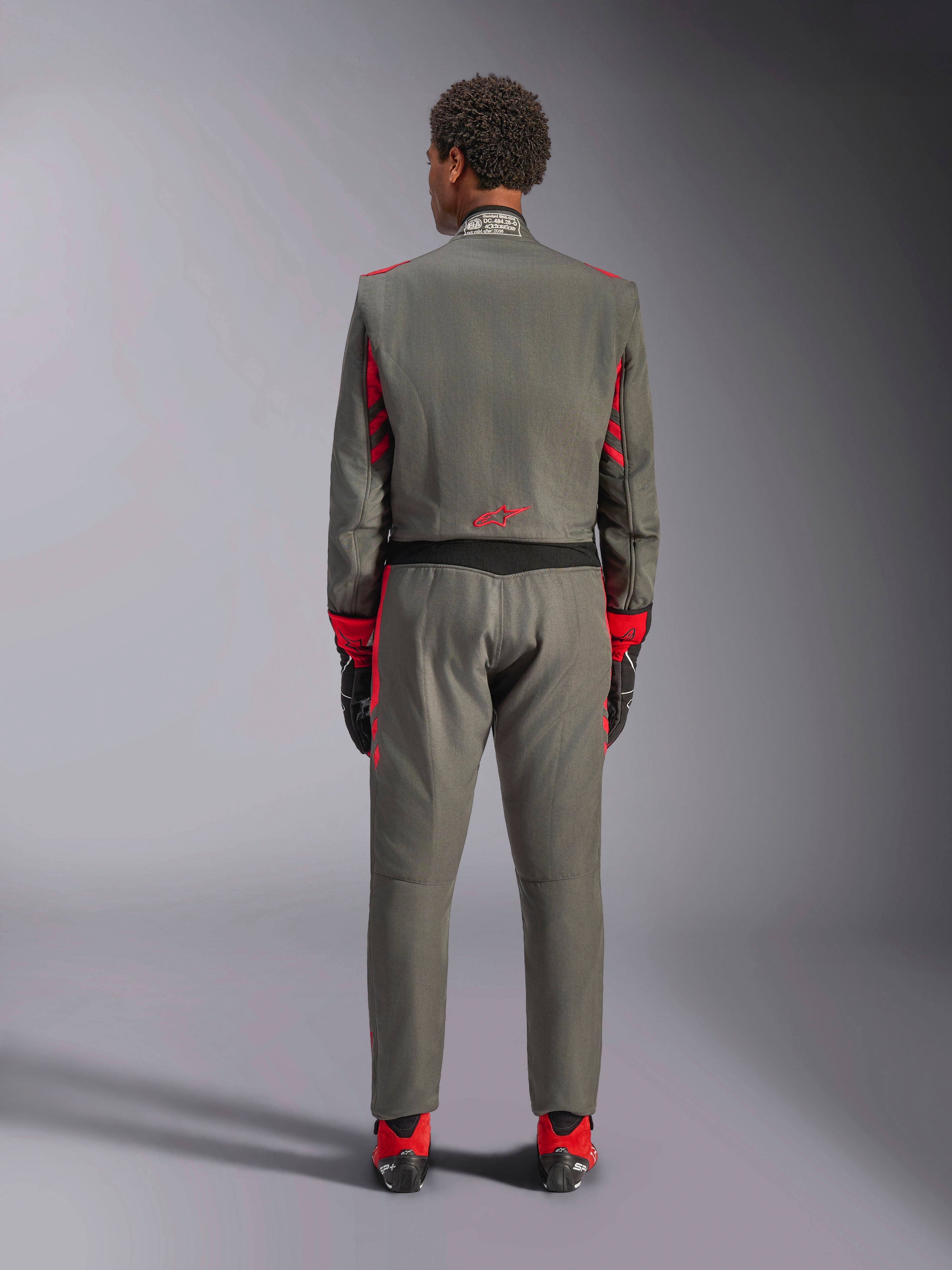 Vista posteriore di un modello che indossa la tuta Alpinestars GP Race V3 in Antracite Rosso, tuta professionale da auto racing con dettagli rossi su maniche e gambe, abbinata a stivali da corsa rossi e guanti neri, abbigliamento tecnico da motorsport in studio.