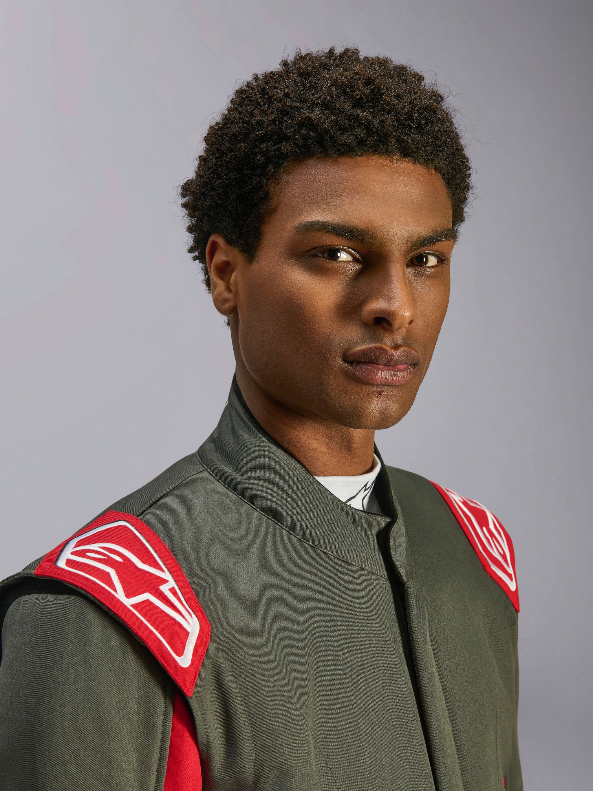 Alpinestars GP Race V3 Suit FIA, tuta da corsa auto, Antracite Rosso, primo piano della parte superiore del busto e della testa, caratterizzata da spalline rosse con logo Alpinestars bianco, colletto alto e materiale in twill grigio