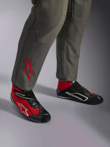 Alpinestars GP Race V3 Suit FIA, tuta da corsa Antracite Rosso, primo piano della parte inferiore delle gambe con logo a stella rosso ricamato, abbinata a stivali da corsa rossi e neri, abbigliamento automobilistico professionale progettato per la protezione e il comfort del pilota