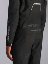 Primo piano della tuta Alpinestars Hypertech V3 in Black/Dark Shadow, con grafiche posteriori 'RACING AHEAD' e 'HYPERTECH V3', logo bianco sulla manica, abbigliamento professionale per corse automobilistiche.
