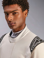 Primo piano di un modello che indossa la tuta Alpinestars Hypertech V3 in bianco nero argento, con colletto alto e chiusura sicura e loghi Alpinestars sulle spalle, abbigliamento professionale per corse automobilistiche.