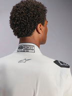 Tuta Alpinestars Hypertech V3, bianca, vista dettagliata del colletto posteriore e della spalla, con etichetta di certificazione FIA 8856-2018, logo Alpinestars grigio stampato e maniglia di estrazione nera, abbigliamento da corsa professionale