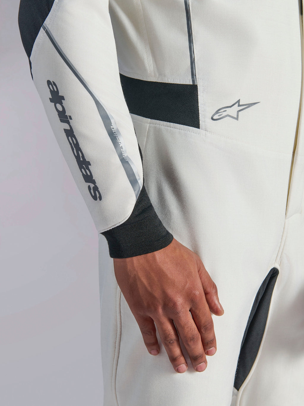 Tuta Alpinestars Hypertech V3, primo piano di una tuta da auto racing bianca con dettagli neri e argento, logo Alpinestars sull'avambraccio, polsino in maglia nera e pannelli elasticizzati scuri per la mobilità, abbigliamento professionale per motorsport.