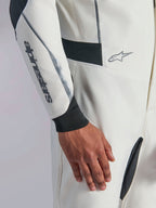 Tuta Alpinestars Hypertech V3, primo piano di una tuta da auto racing bianca con dettagli neri e argento, logo Alpinestars sull'avambraccio, polsino in maglia nera e pannelli elasticizzati scuri per la mobilità, abbigliamento professionale per motorsport.