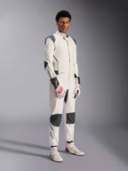 Modello che indossa la tuta Alpinestars Hypertech V3, bianco con accenti neri e argento, abbigliamento professionale per corse automobilistiche con pannelli neri su spalle e ginocchia, abbinata a guanti da corsa bianchi e rossi e stivali da corsa bianchi