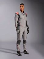 Modello che indossa la tuta Alpinestars Hypertech V3 in grigio medio con accenti neri e rosso fluo, tuta da corsa professionale abbinata a guanti e scarpe da racing neri, con struttura leggera in Nomex a due strati, dettagli rossi sulle spalle e vestibilità atletica