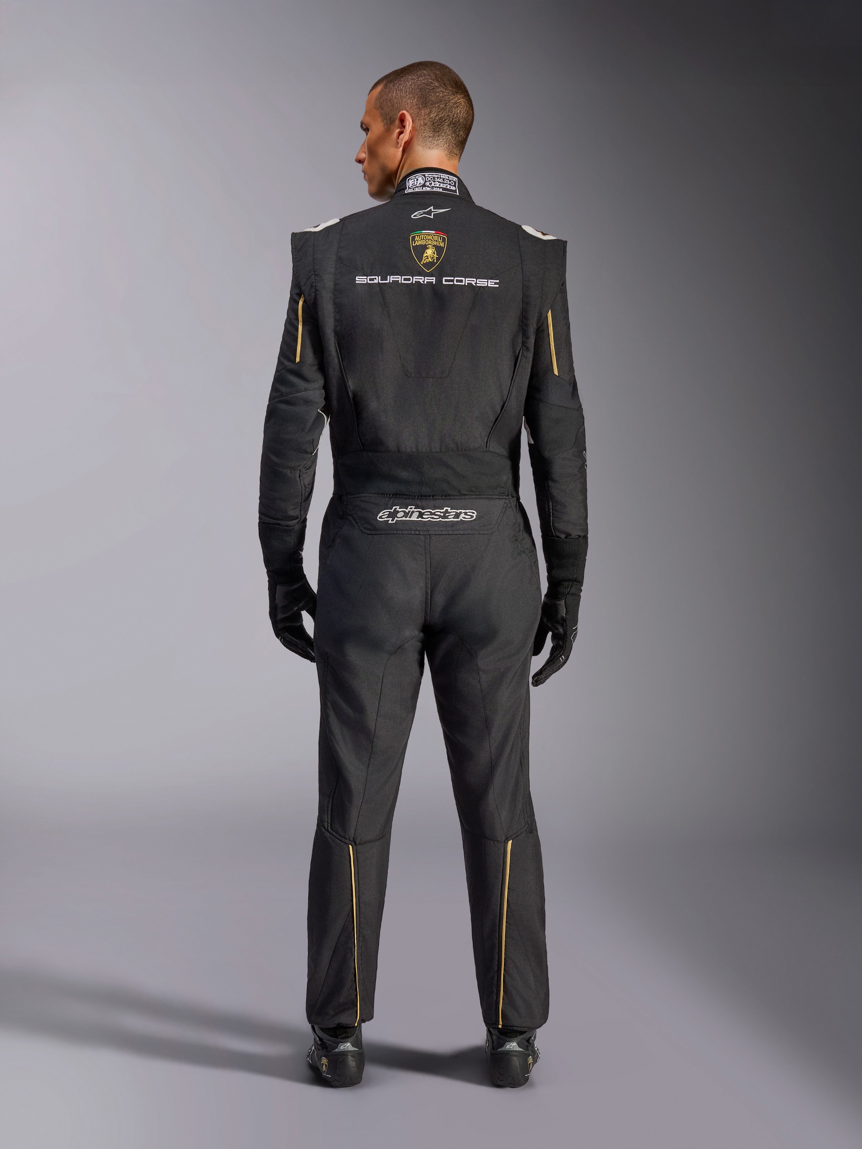 Alpinestars Edizione Limitata Lamborghini GP Tech V4 Suit FIA, tuta da corsa automobilistica, nera con accenti oro e argento, vista posteriore con marchio Lamborghini Squadra Corse, logo Alpinestars e bordini dorati su maniche e gambe, abbigliamento tecnico professionale