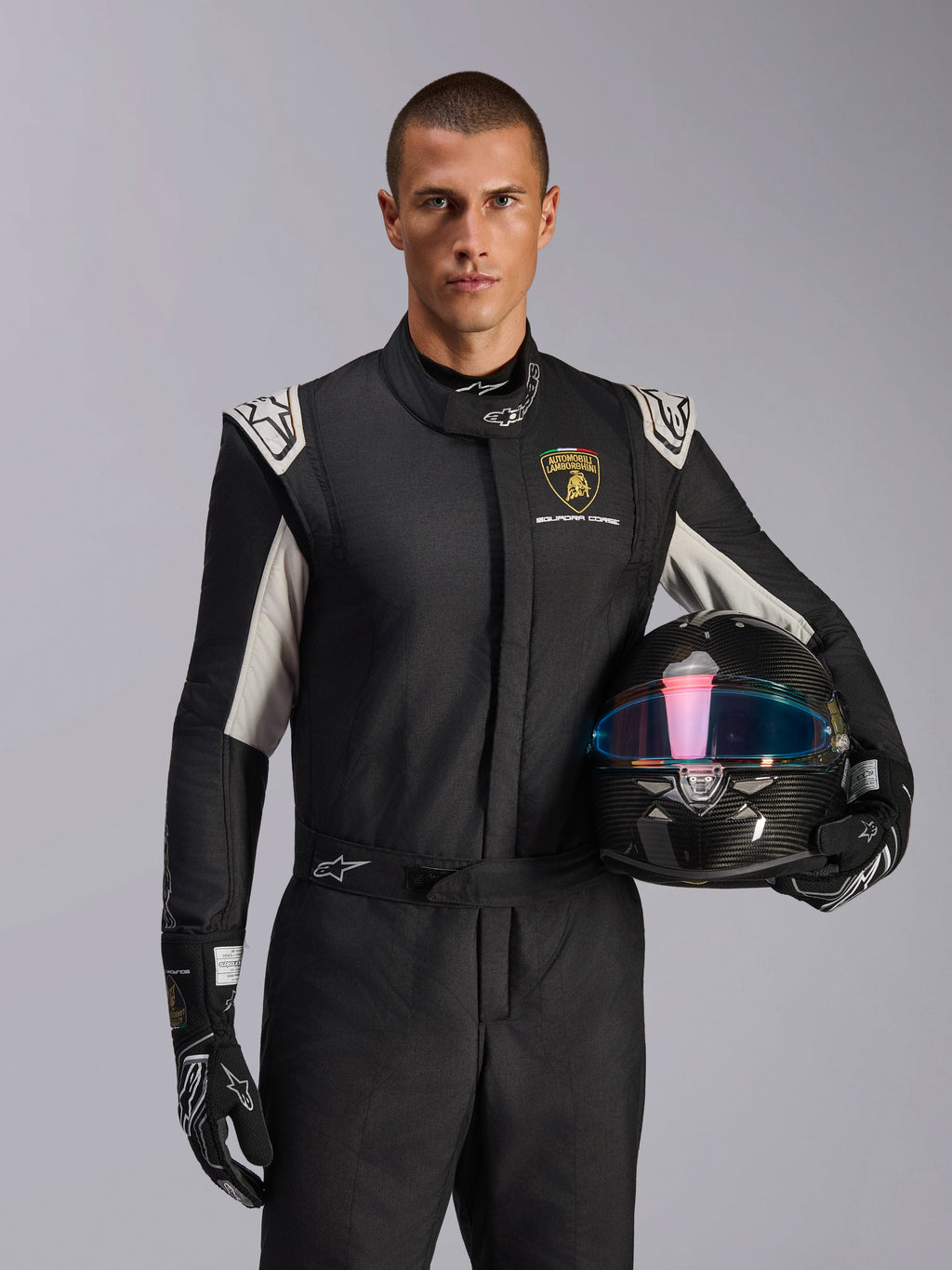 Modello con tuta Limited Edition Lamborghini GP Tech V4, tuta da corsa nera con dettagli argento e logo Lamborghini Squadra Corse, casco in fibra di carbonio, guanti da corsa neri con loghi bianchi, equipaggiamento professionale per corse automobilistiche