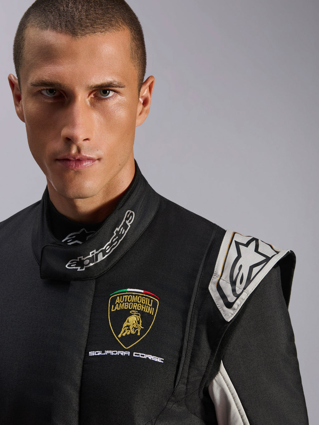 Tuta Alpinestars Limited Edition Lamborghini GP Tech V4, tuta da corsa professionale, nera con accenti argento e oro, primo piano con logo Lamborghini Squadra Corse sul petto e marchio Alpinestars sul collo, protezione premium per il motorsport