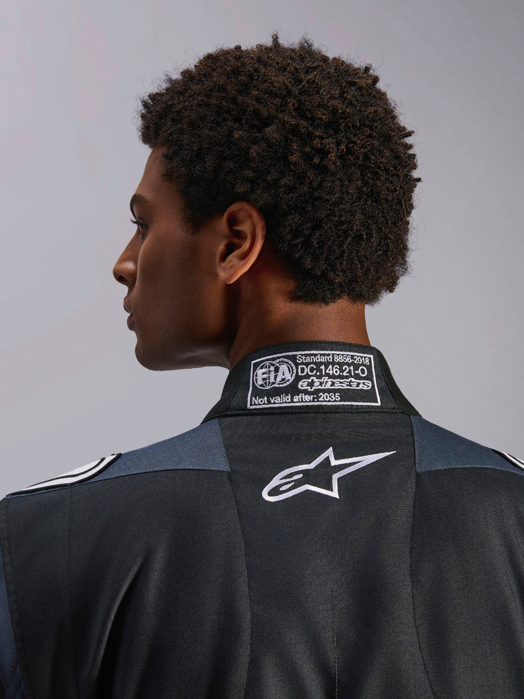 Alpinestars tuta GP Pro Comp V2 FIA, tuta da auto da uomo, nera e asfalto, dettaglio del colletto posteriore con certificazione FIA 8856-2018 e logo Astar bianco.
