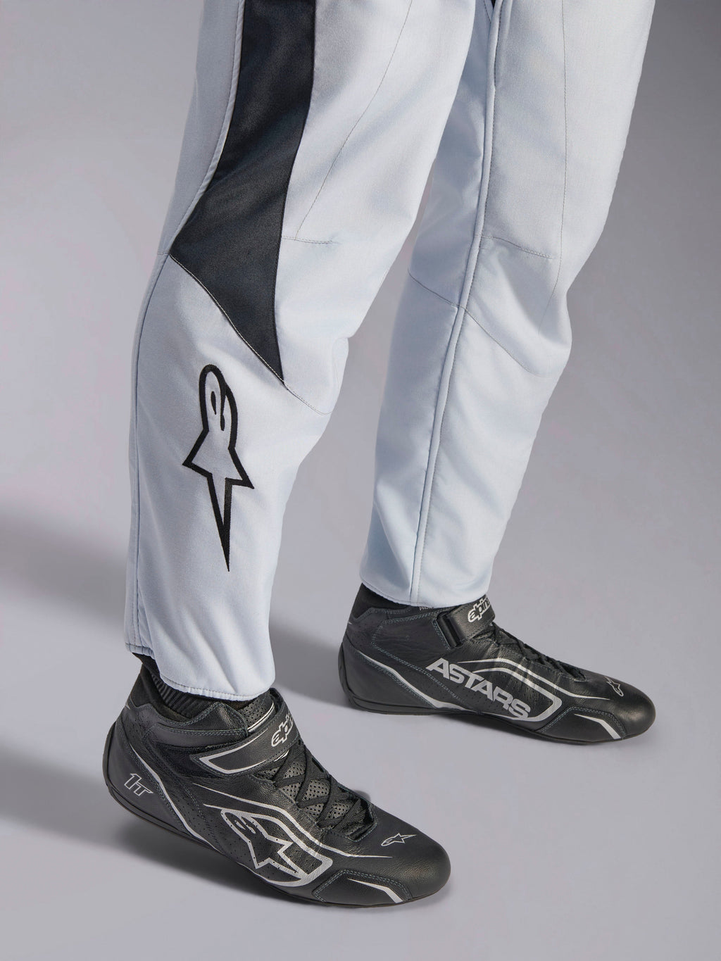 Tuta Alpinestars GP Pro Comp V2 FIA grigia e nera, dettaglio gamba con logo a stella e stivaletti da corsa neri.