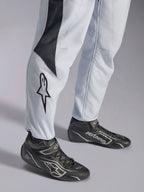 Tuta Alpinestars GP Pro Comp V2 FIA grigia e nera, dettaglio gamba con logo a stella e stivaletti da corsa neri.
