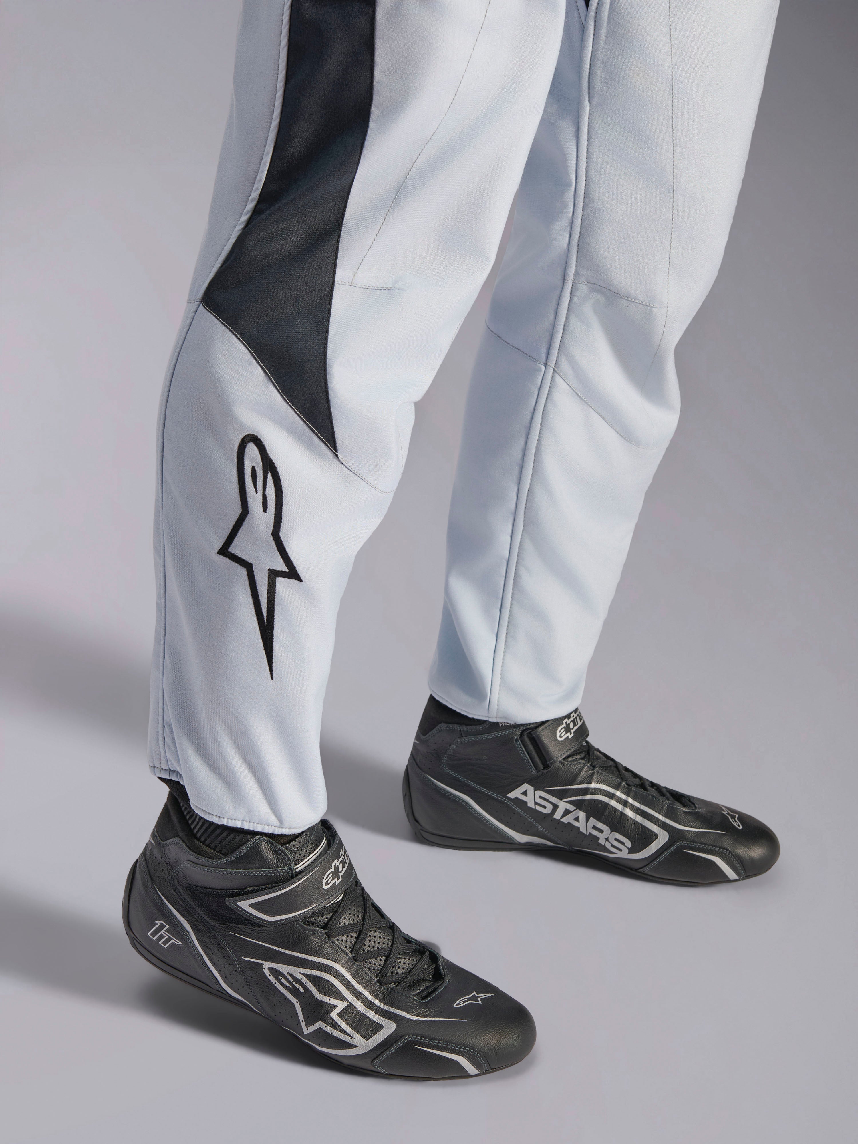 Tuta Alpinestars GP Pro Comp V2 FIA grigia e nera, dettaglio gamba con logo a stella e stivaletti da corsa neri.