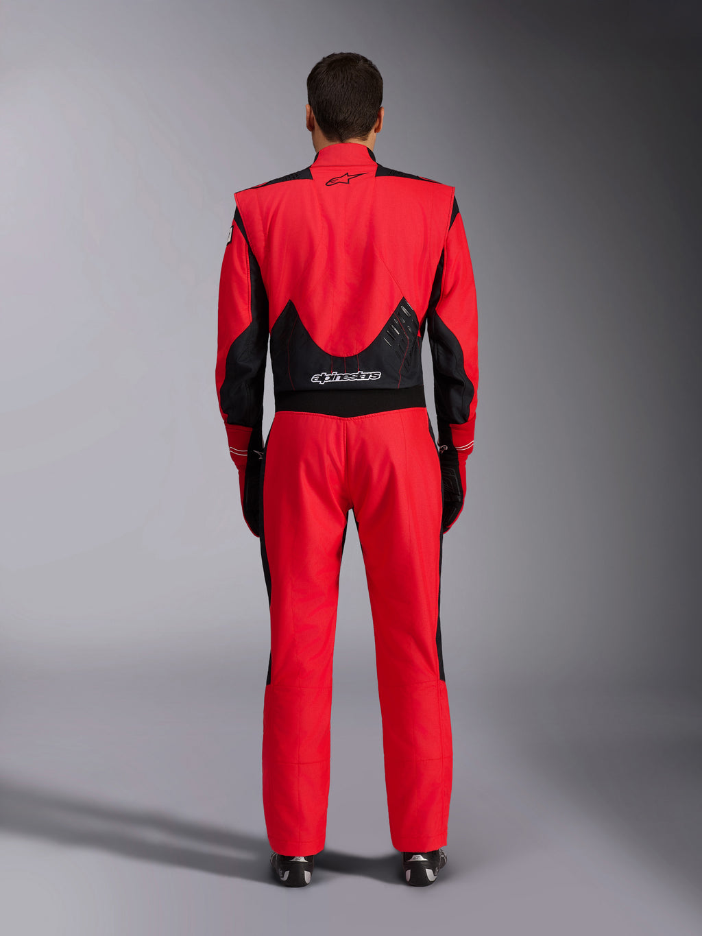 Tuta da gara Alpinestars GP Pro Comp V2 FIA, rosso e nero, vista posteriore con rete nera e pannelli elasticizzati sulla parte bassa della schiena, marchio Alpinestars sulla parte superiore e inferiore della schiena, abbigliamento professionale per corse automobilistiche