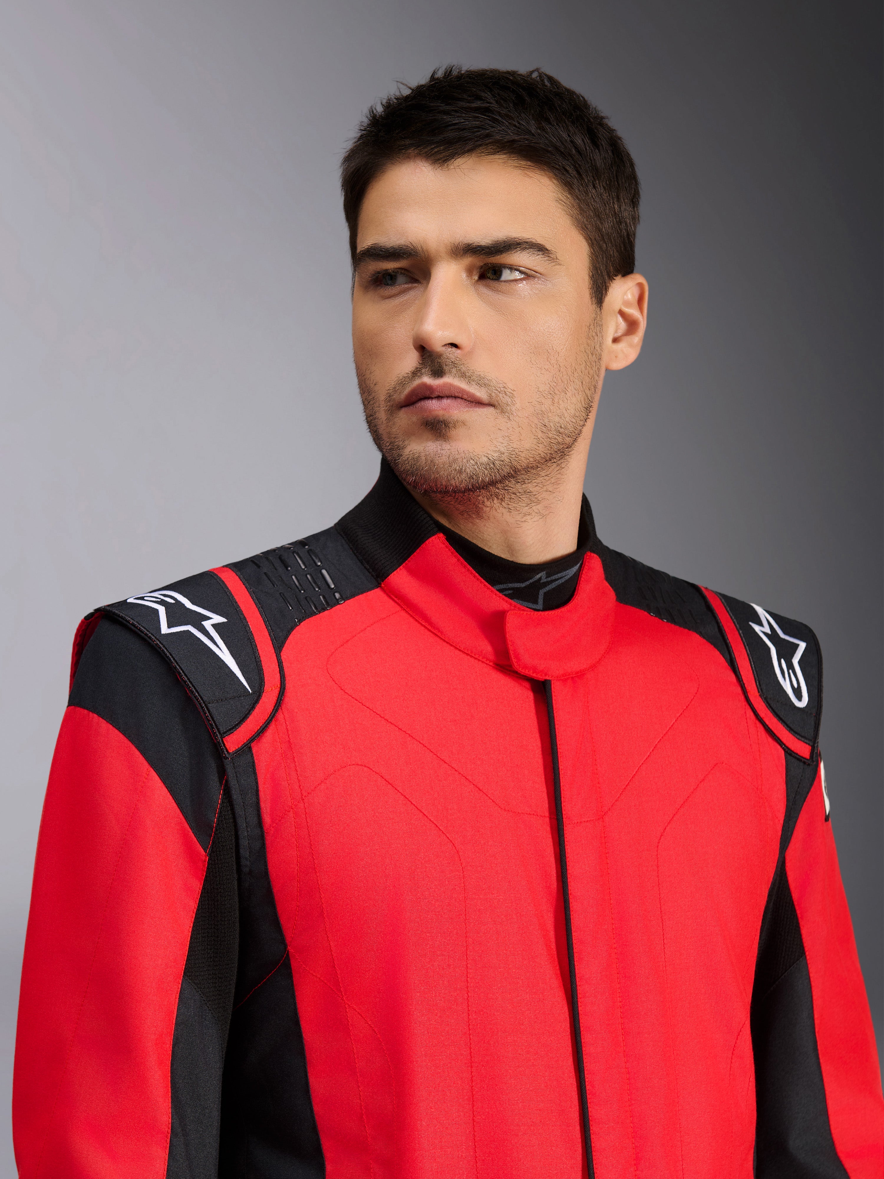 Modello che indossa la tuta auto Alpinestars GP Pro Comp V2 FIA, rosso e nero, con loghi Astars bianchi sulle spalle e dettagli con tecnologia grip in silicone, abbigliamento professionale per motorsport