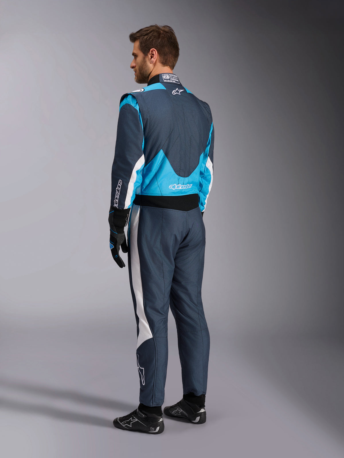 Alpinestars GP Pro Comp V2 FIA, tuta da corsa auto, grigio asfalto e blu ciano, vista posteriore su modello, omologata FIA.