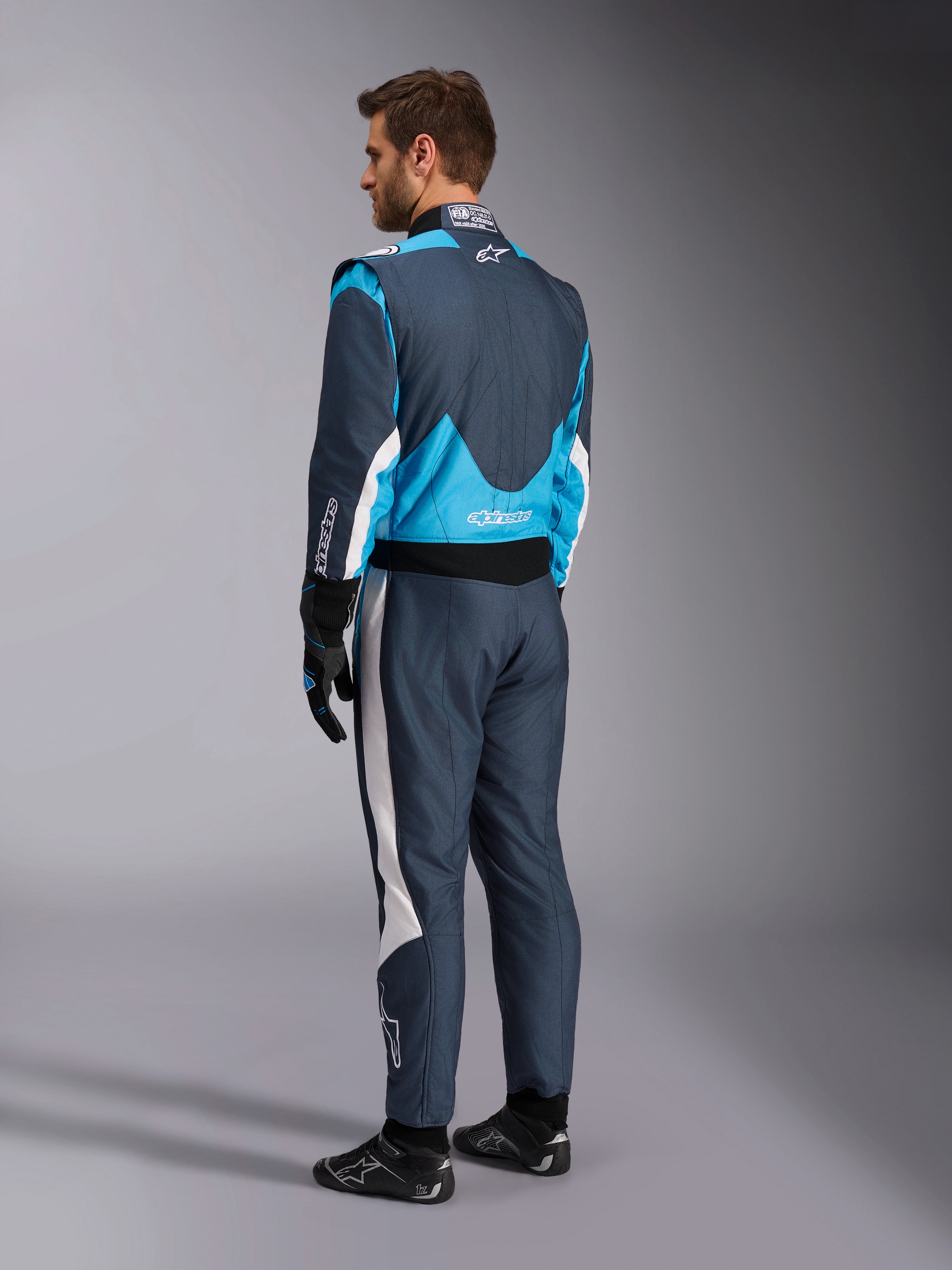 Alpinestars GP Pro Comp V2 FIA, tuta da corsa auto, grigio asfalto e blu ciano, vista posteriore su modello, omologata FIA.